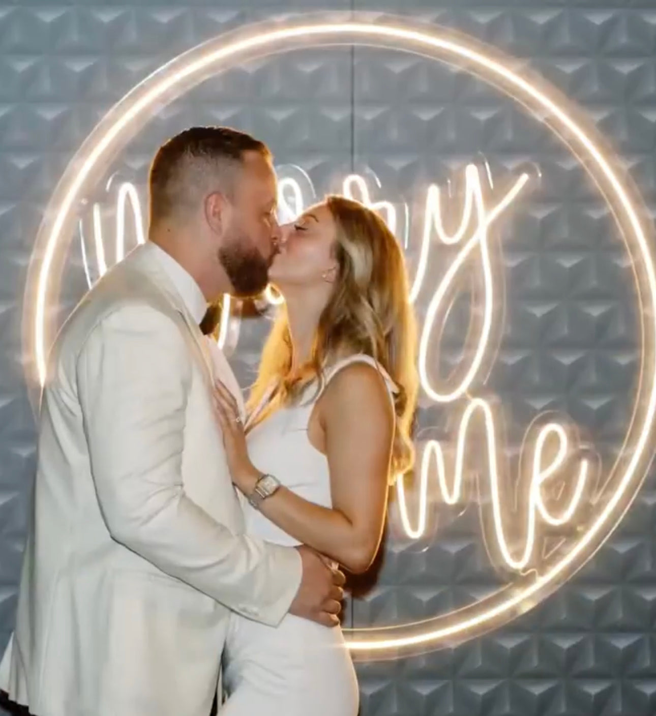 a man and woman kissing in front of a neon sign